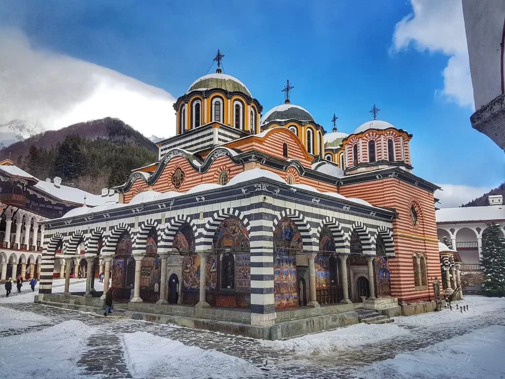 Рилският манастир в снега с раираните аркади и куполите